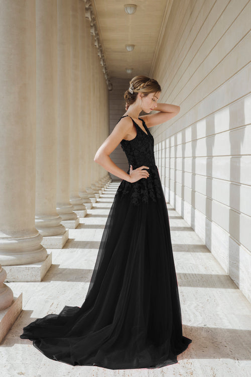 Woman in a black dress standing in a sunlit colonnade