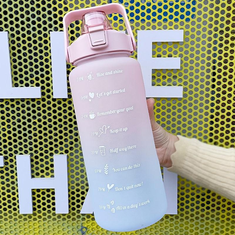 Pink and blue motivational water bottle held by a hand against a yellow background with large white letters.
