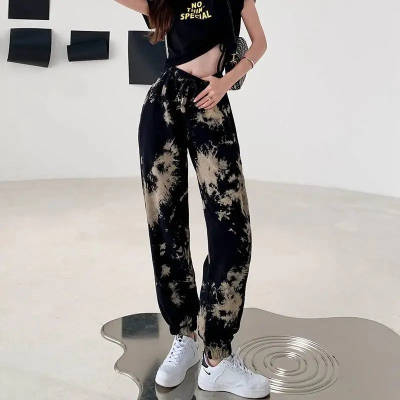 Person wearing a black and beige tie-dye outfit with white sneakers on a minimalistic background