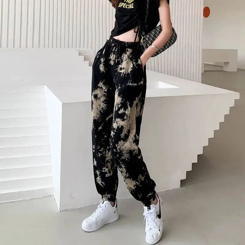 Person wearing tie-dye pants and white sneakers in a minimalistic setting