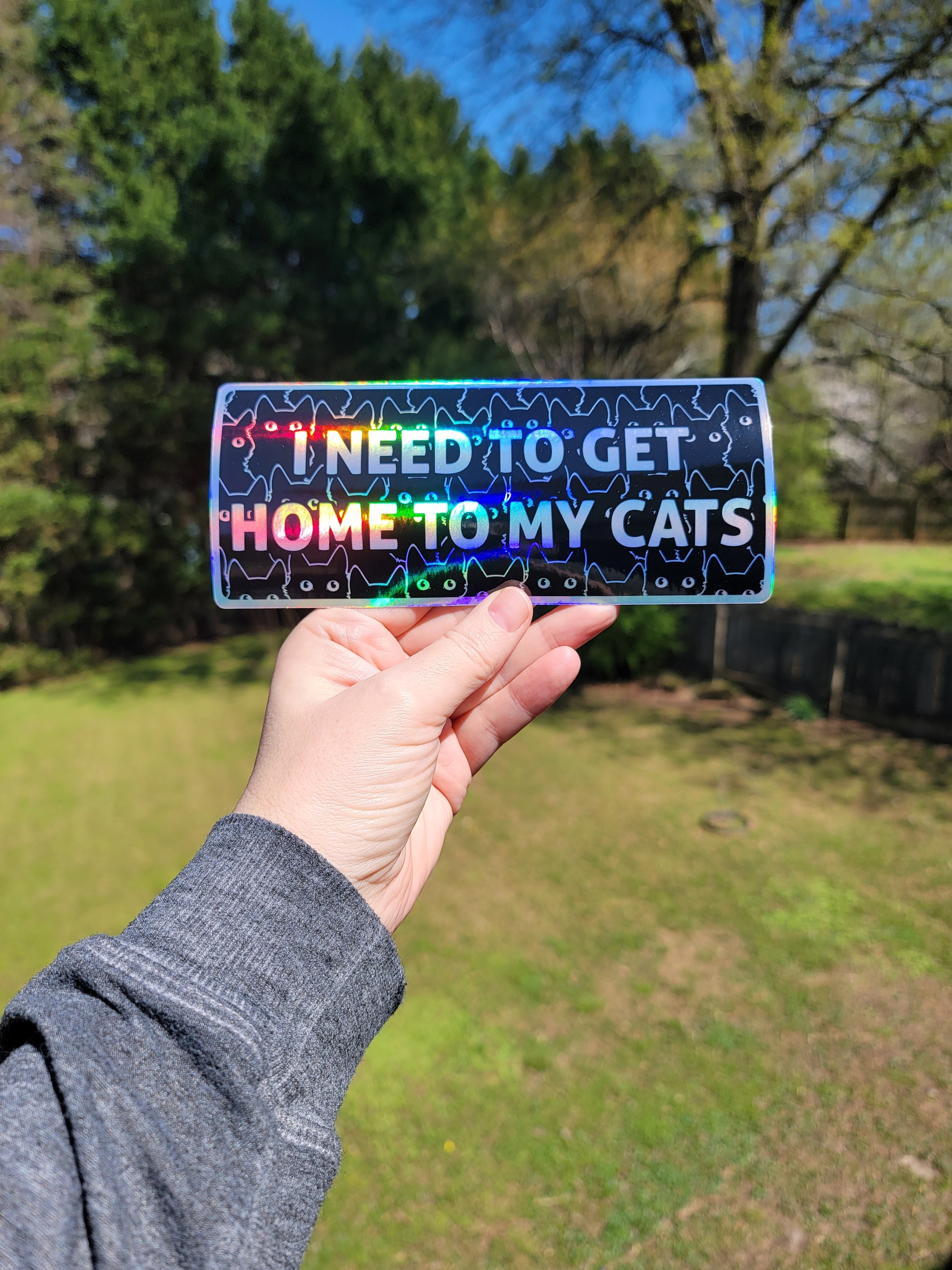 Hand holding a colorful bumper sticker with text outdoors