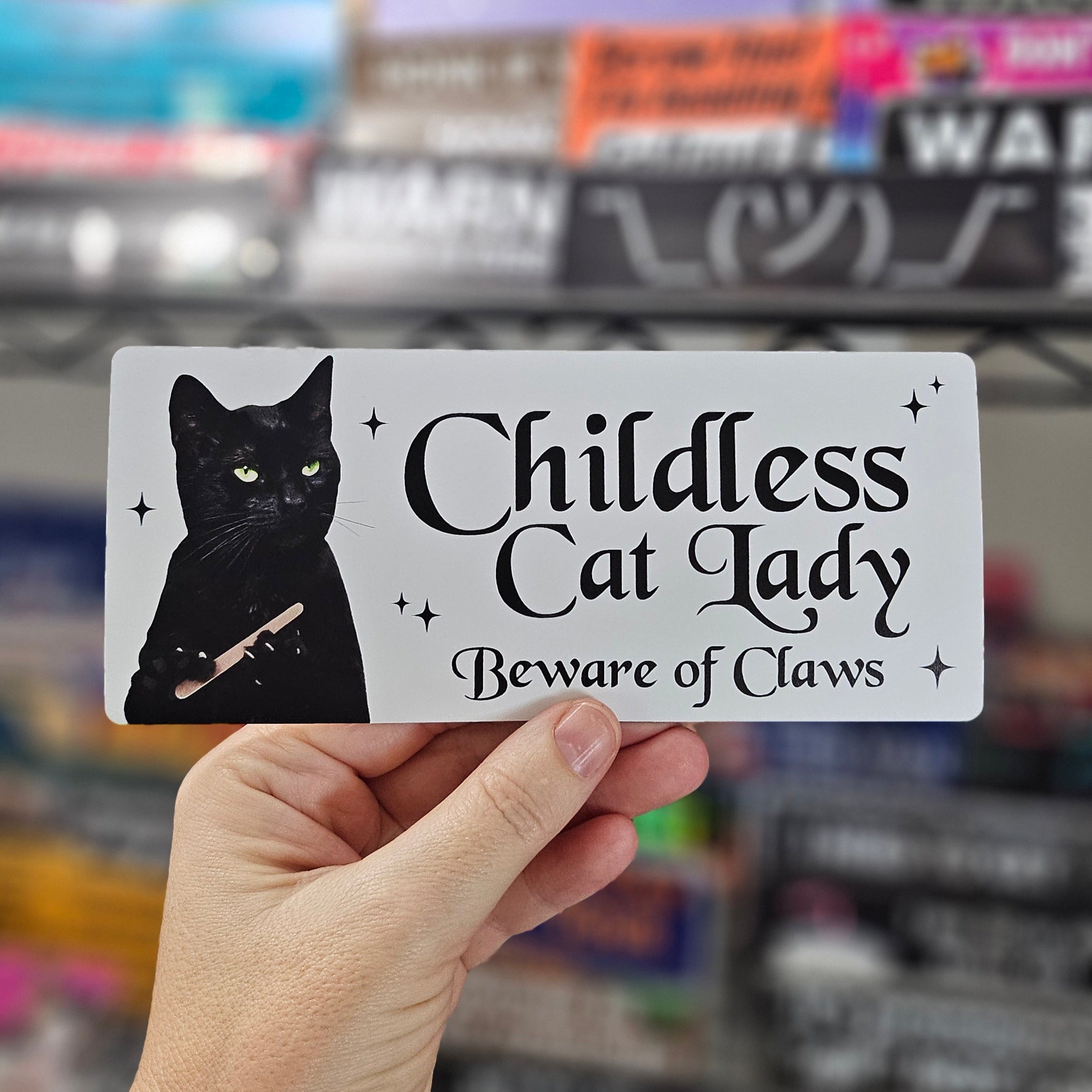 Hand holding a sign with a black cat illustration and text in front of a store shelf.