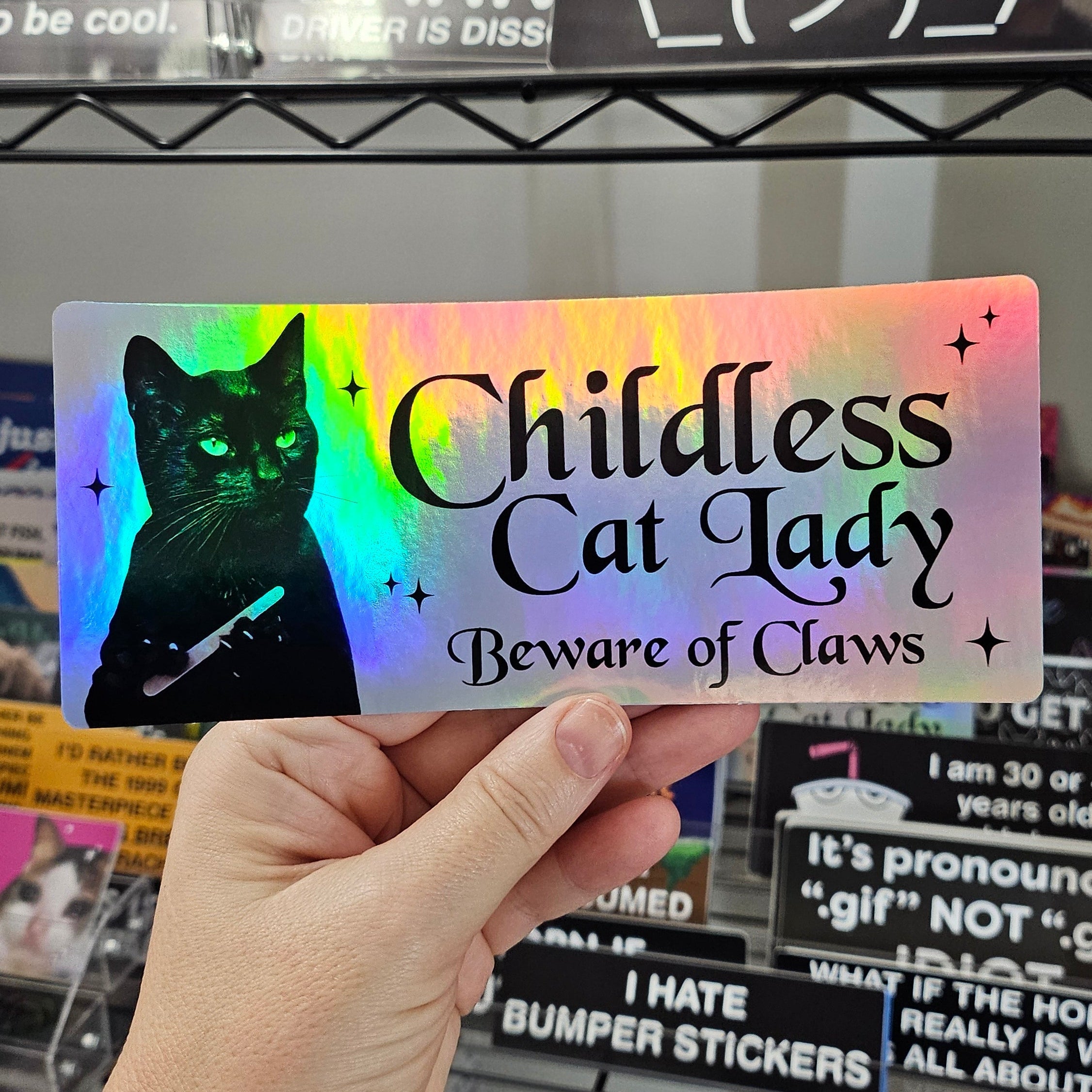Holographic bumper sticker with a cat design and text held by a hand.