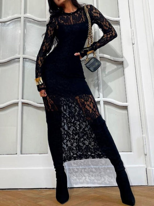 Person wearing a black lace dress with long sleeves and a matching handbag against a white paneled wall.