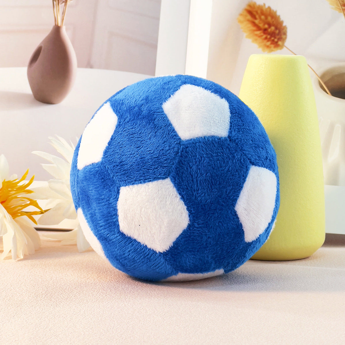 Blue and white plush soccer ball on a light surface with decorative vases in the background