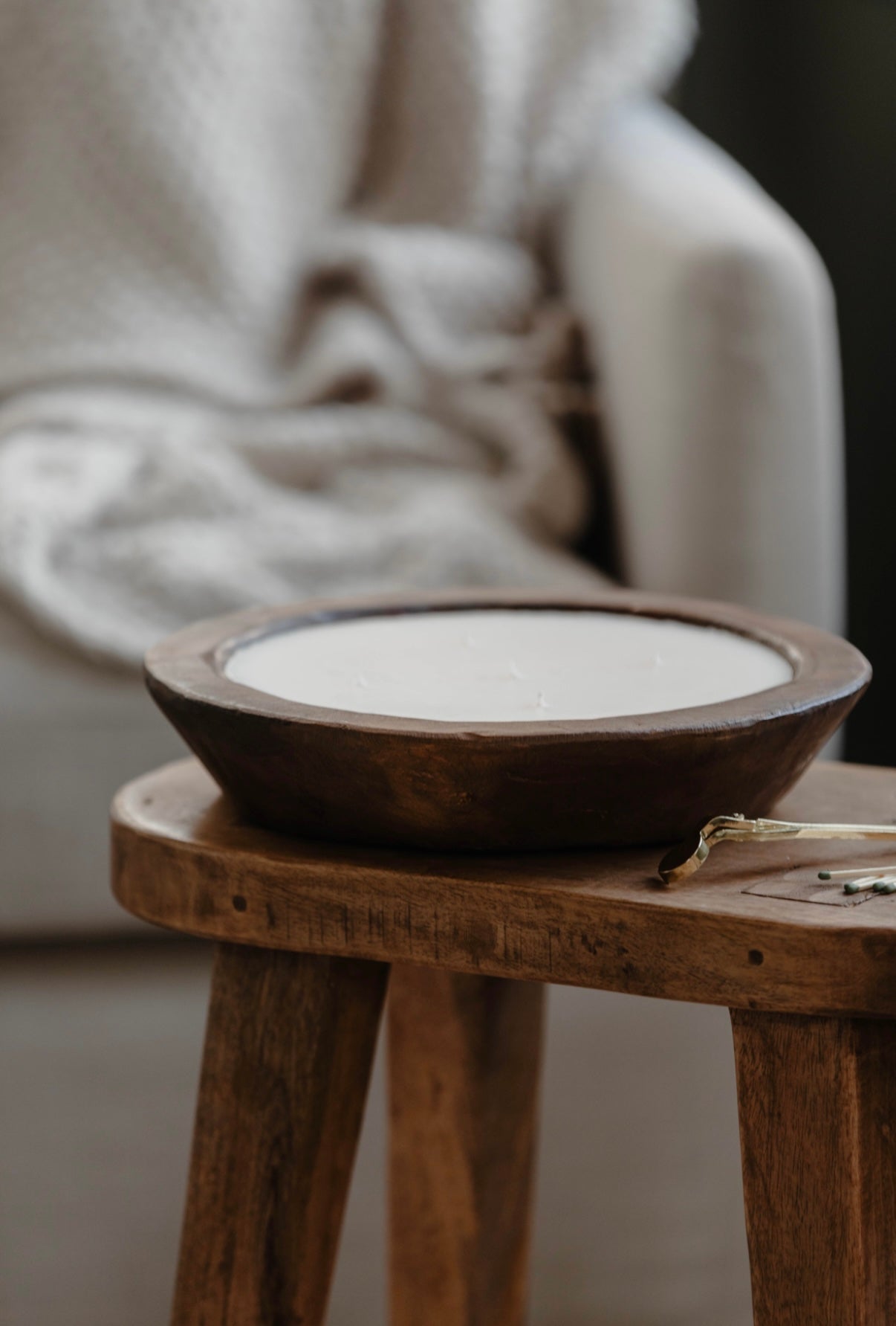 Wooden stool with a round wooden bowl on top, blurred background