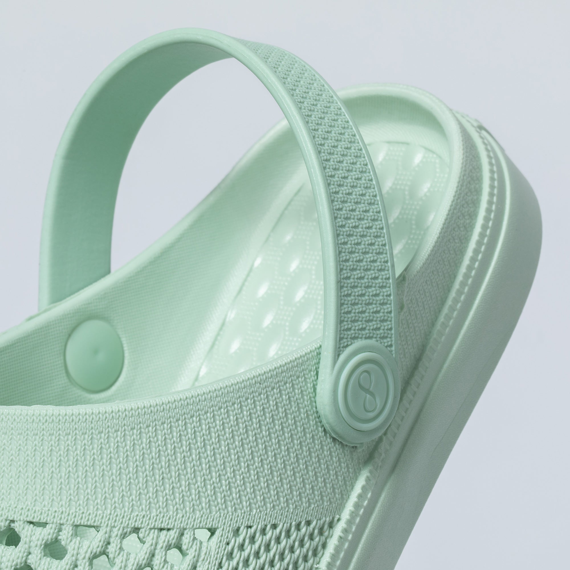 Light green sandal with textured strap on a light gray background