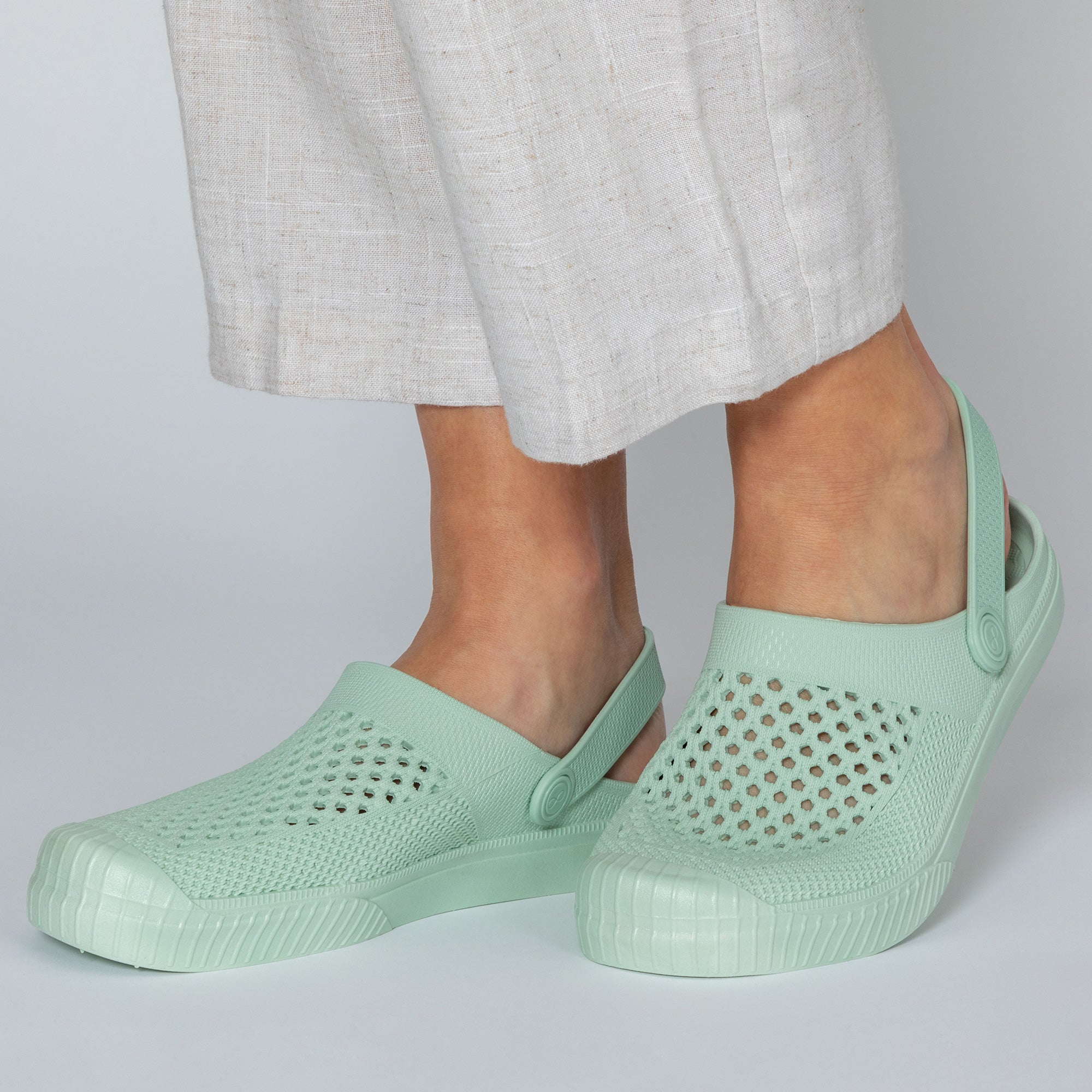 Light green clogs worn with light gray pants on a plain background