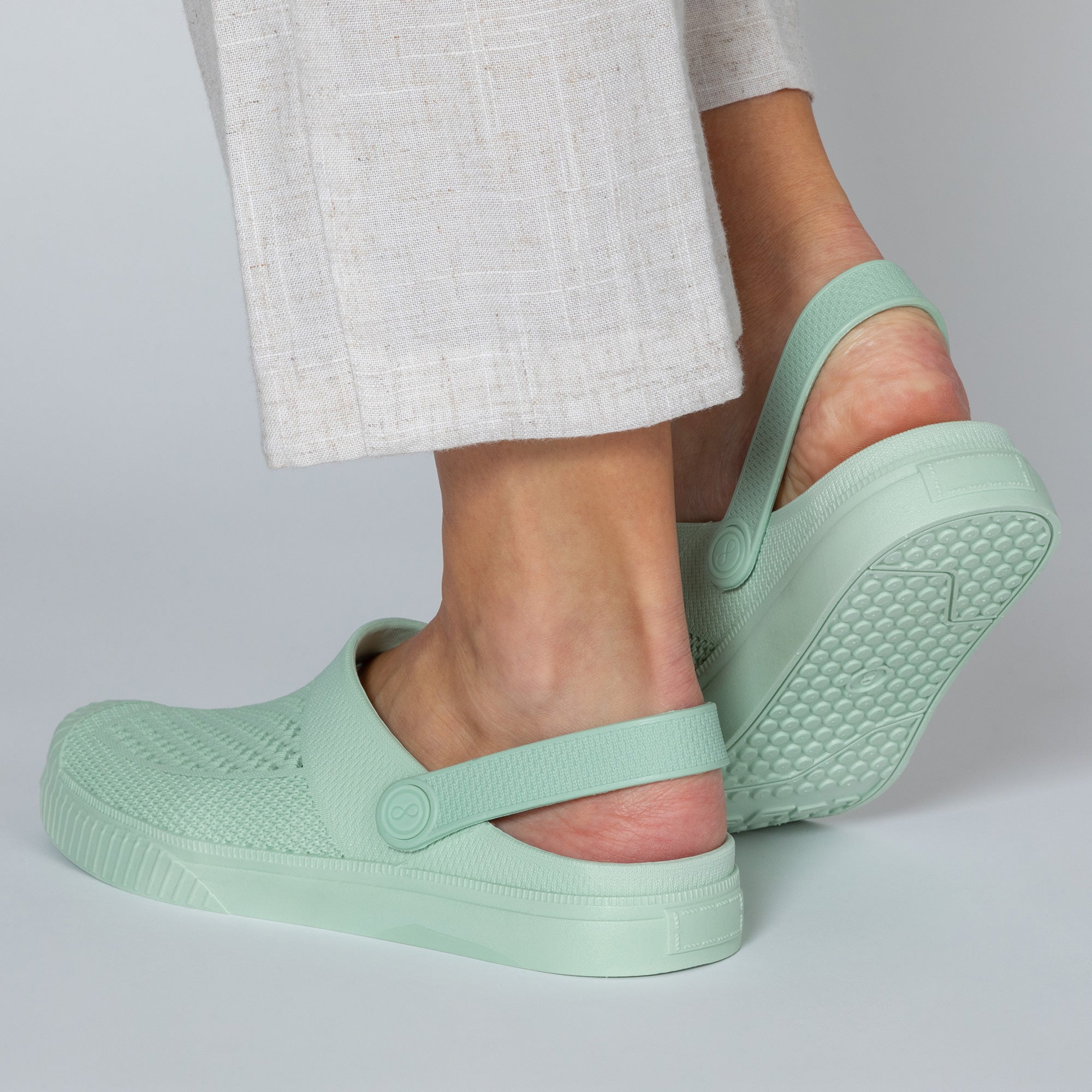 Light green clogs worn with light gray pants on a neutral background