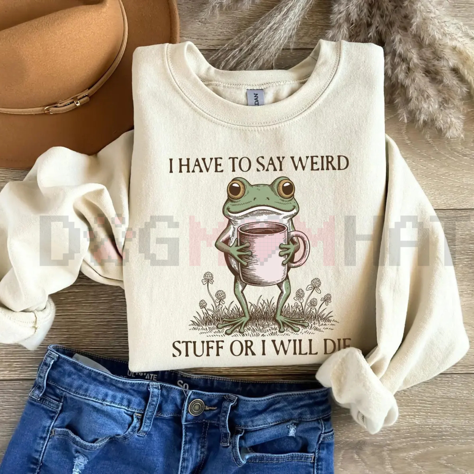 Beige sweatshirt with a frog graphic and text on a wooden surface