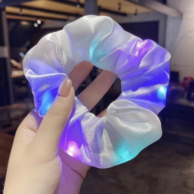 Hand holding a glowing LED scrunchie with a blurred indoor background