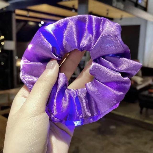 Purple scrunchie held by a hand with a blurred indoor background