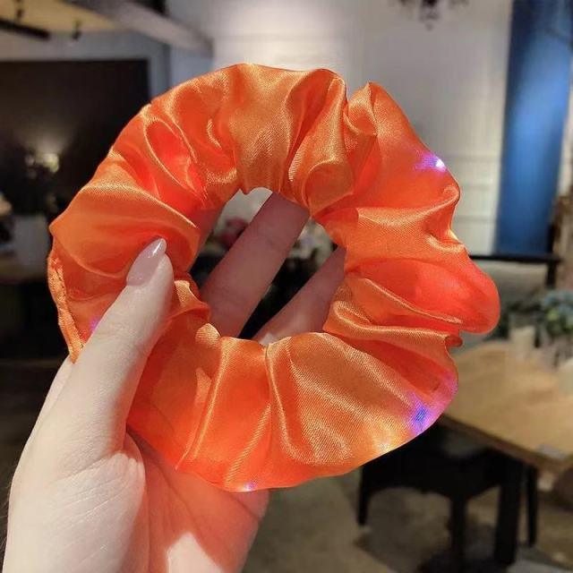 Orange scrunchie held by a hand with a blurred indoor background
