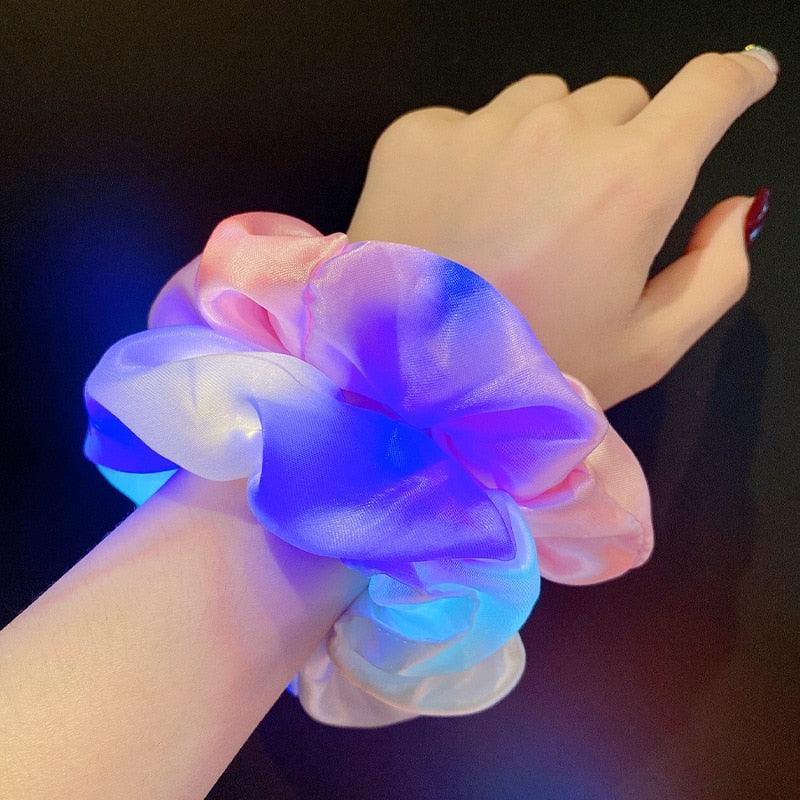 Hand wearing a colorful LED scrunchie on a dark background
