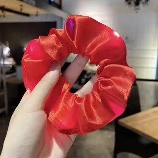 Red hair scrunchie held by a hand with a blurred indoor background