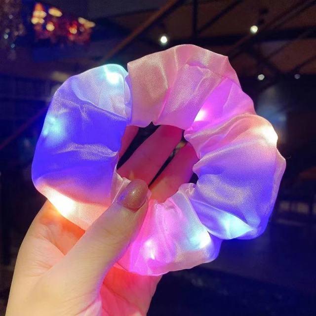 Multicolored LED scrunchie being held in a hand with a blurred indoor background
