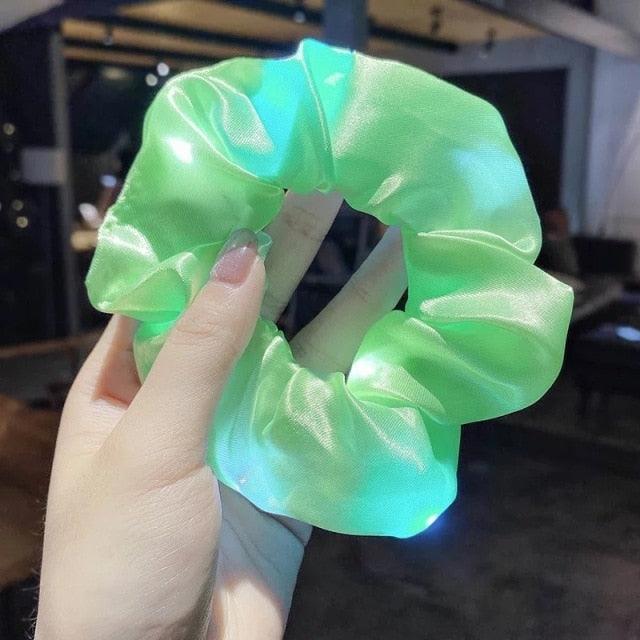 Green glowing scrunchie held by a hand with blurred indoor background