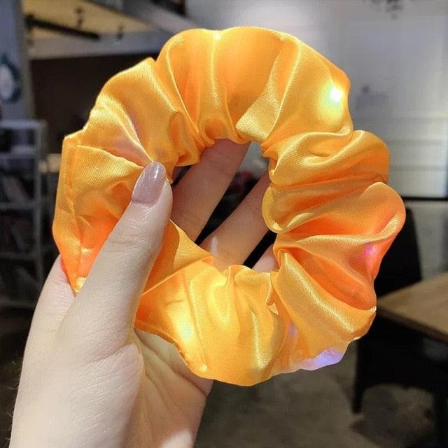 Yellow scrunchie held by a hand with a blurred indoor background