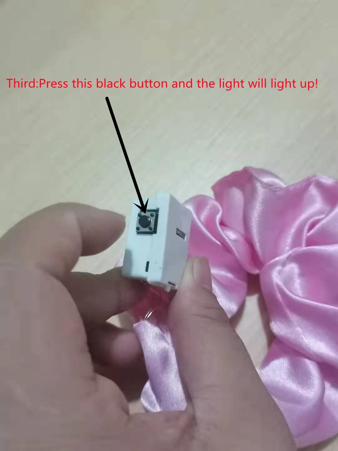 Hand holding a small electronic device with a black button, pink fabric in the background