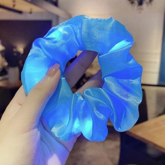 Blue scrunchie held by a hand with a blurred indoor background