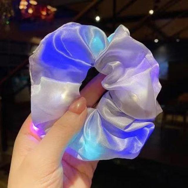 Glowing LED scrunchie held by a hand against a blurred indoor background