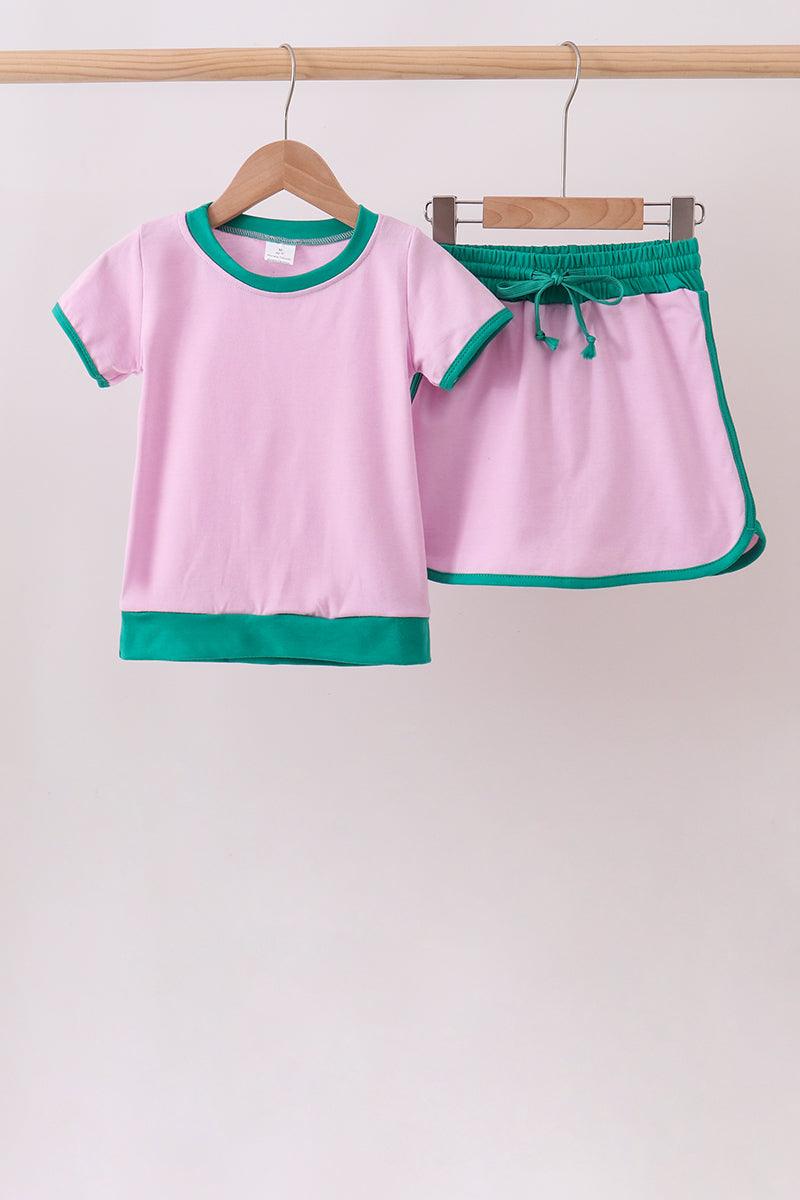 Pink children's outfit with green trim on a hanger against a white background