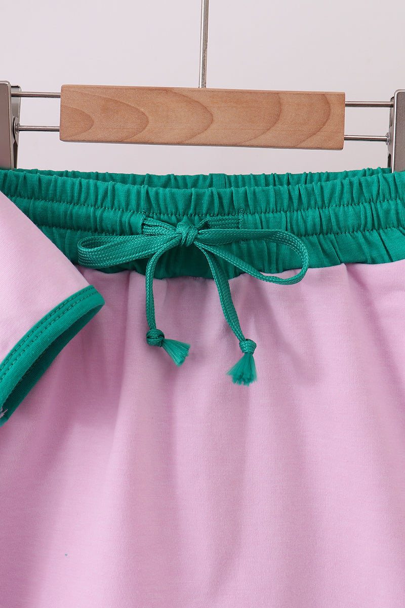 Close-up of a pink garment with green trim on a hanger against a white wall.