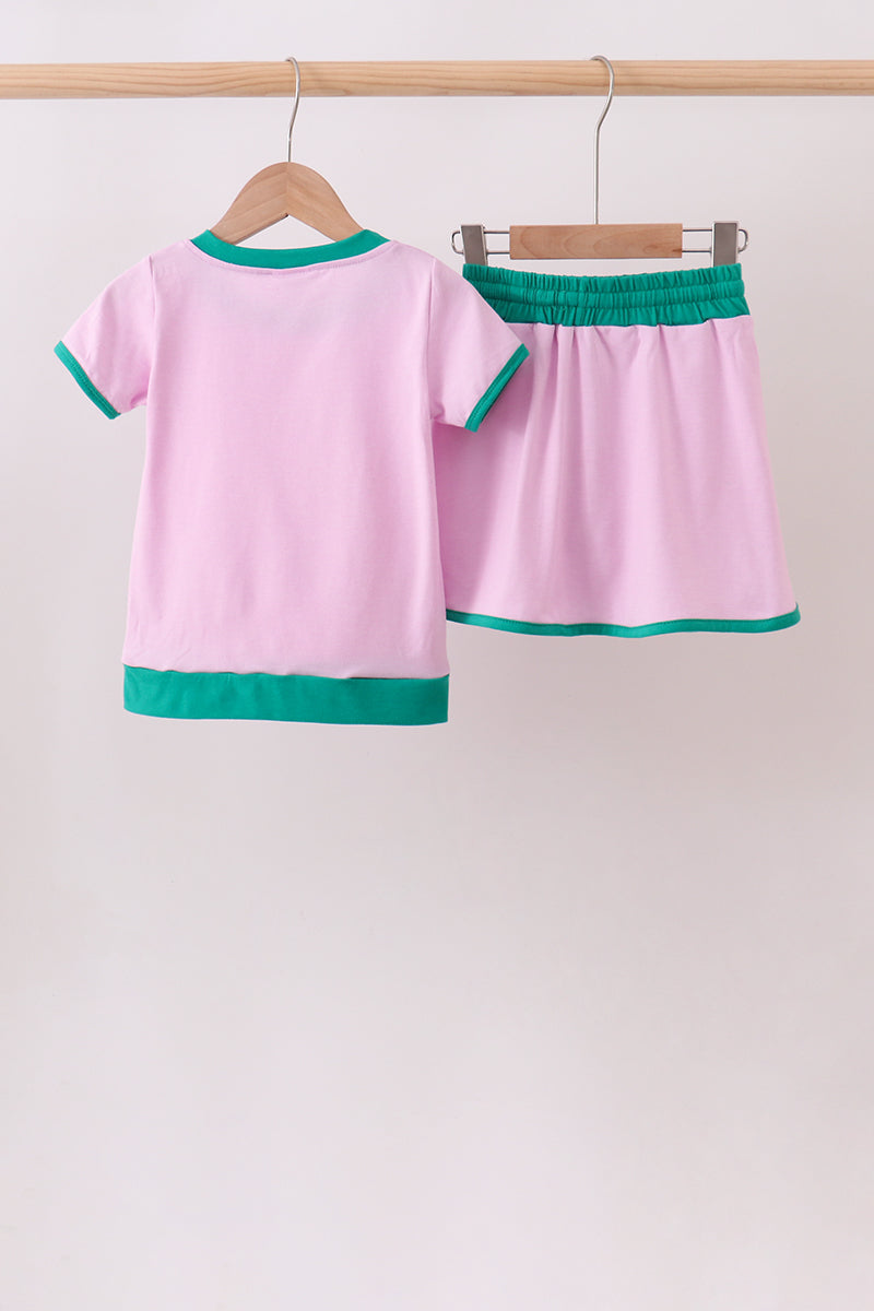 Pink children's outfit with green trim on a wooden hanger against a white background