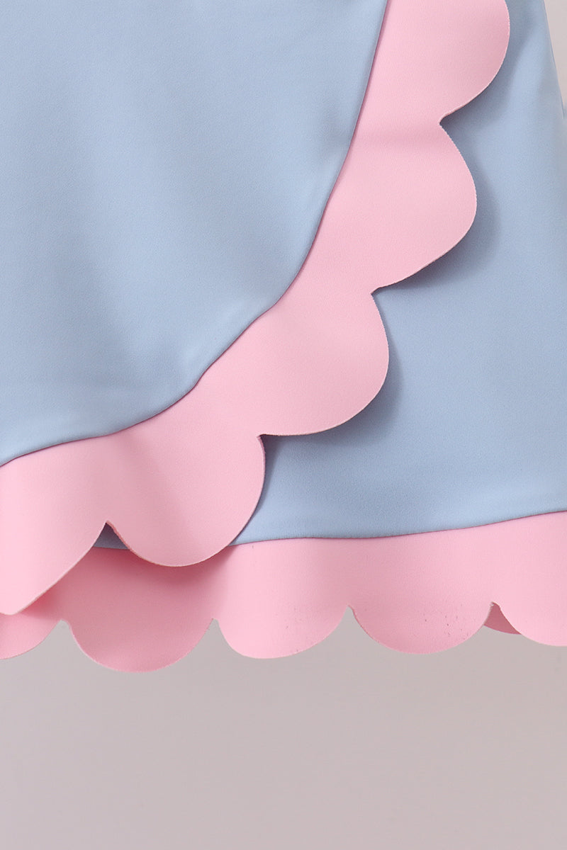 Close-up of a dress with pink scalloped hem on a light gray background