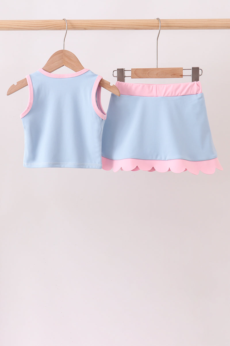 Children's light blue tank top and skirt set with pink trim on a wooden hanger against a beige background.