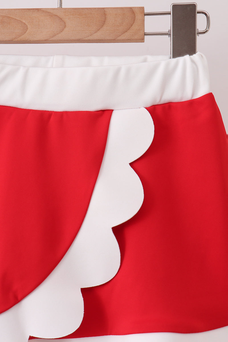 Red and white skirt with scalloped edge on a wooden hanger.