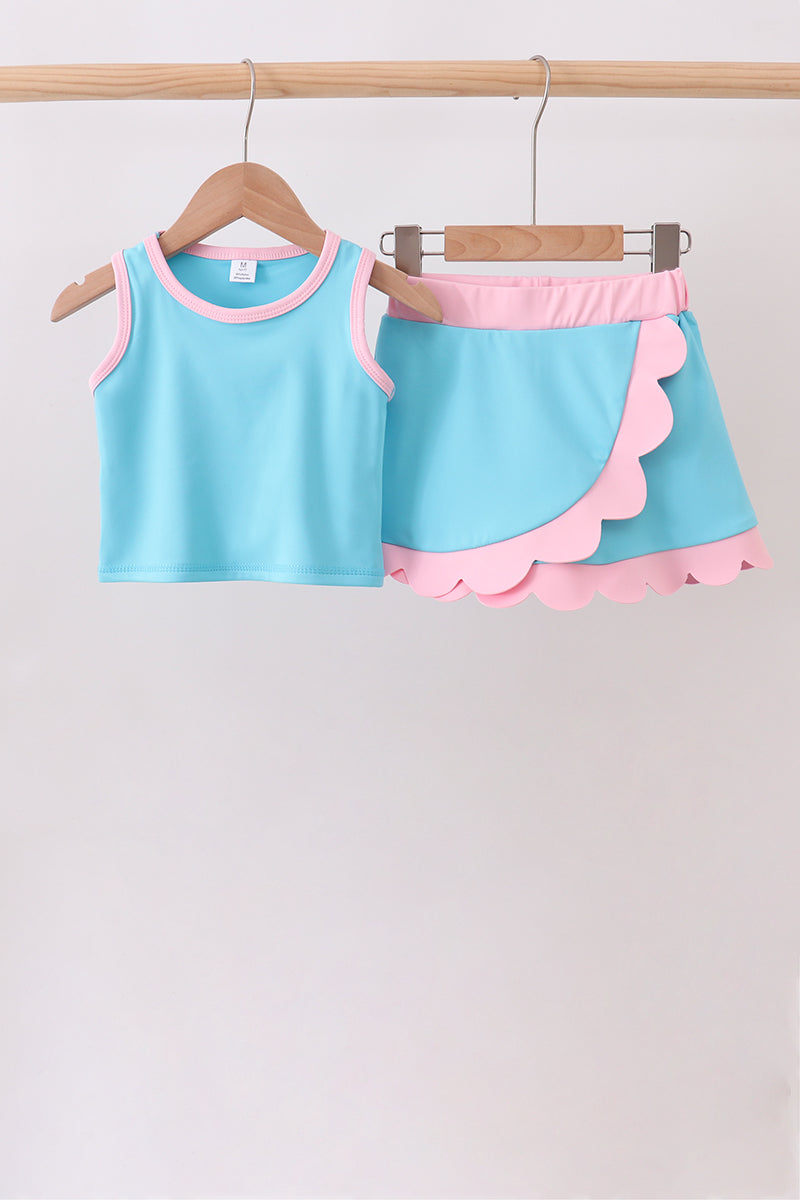 Children's blue and pink outfit with a scalloped skirt on a wooden hanger against a white background.