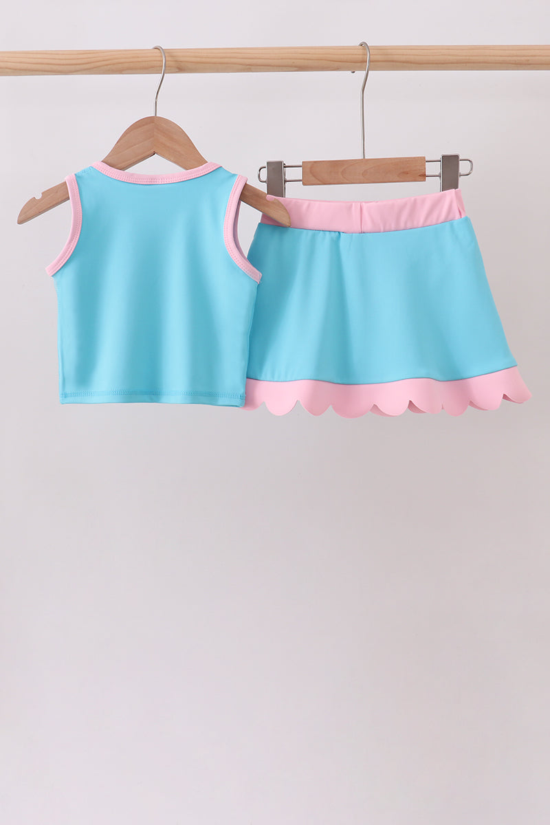 Light blue tank top and pink shorts set on hangers against a plain background