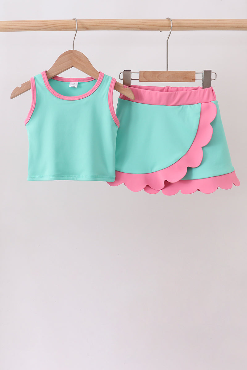 Children's outfit with turquoise top and pink shorts on a wooden hanger against a white background