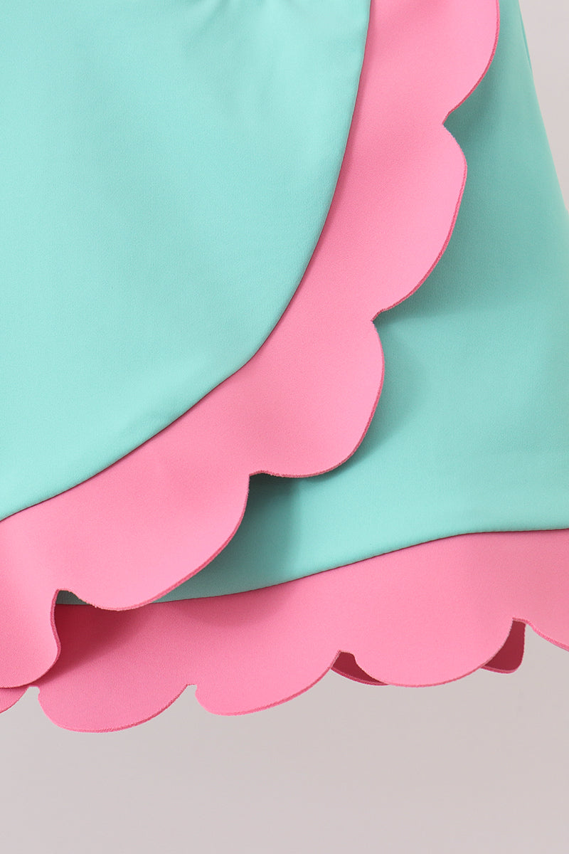 Close-up of pink and turquoise paper with scalloped edges on a light gray background