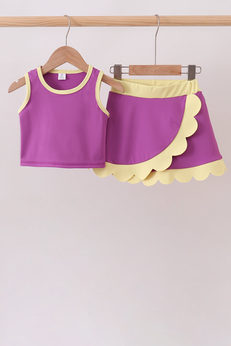 Purple tank top and shorts set with yellow trim on hangers against a light pink background