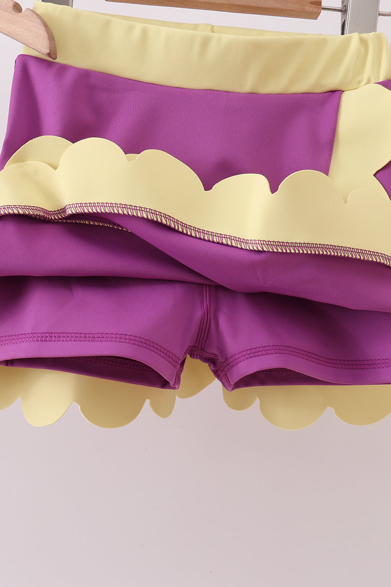 Purple shorts with yellow scalloped edges on a white background