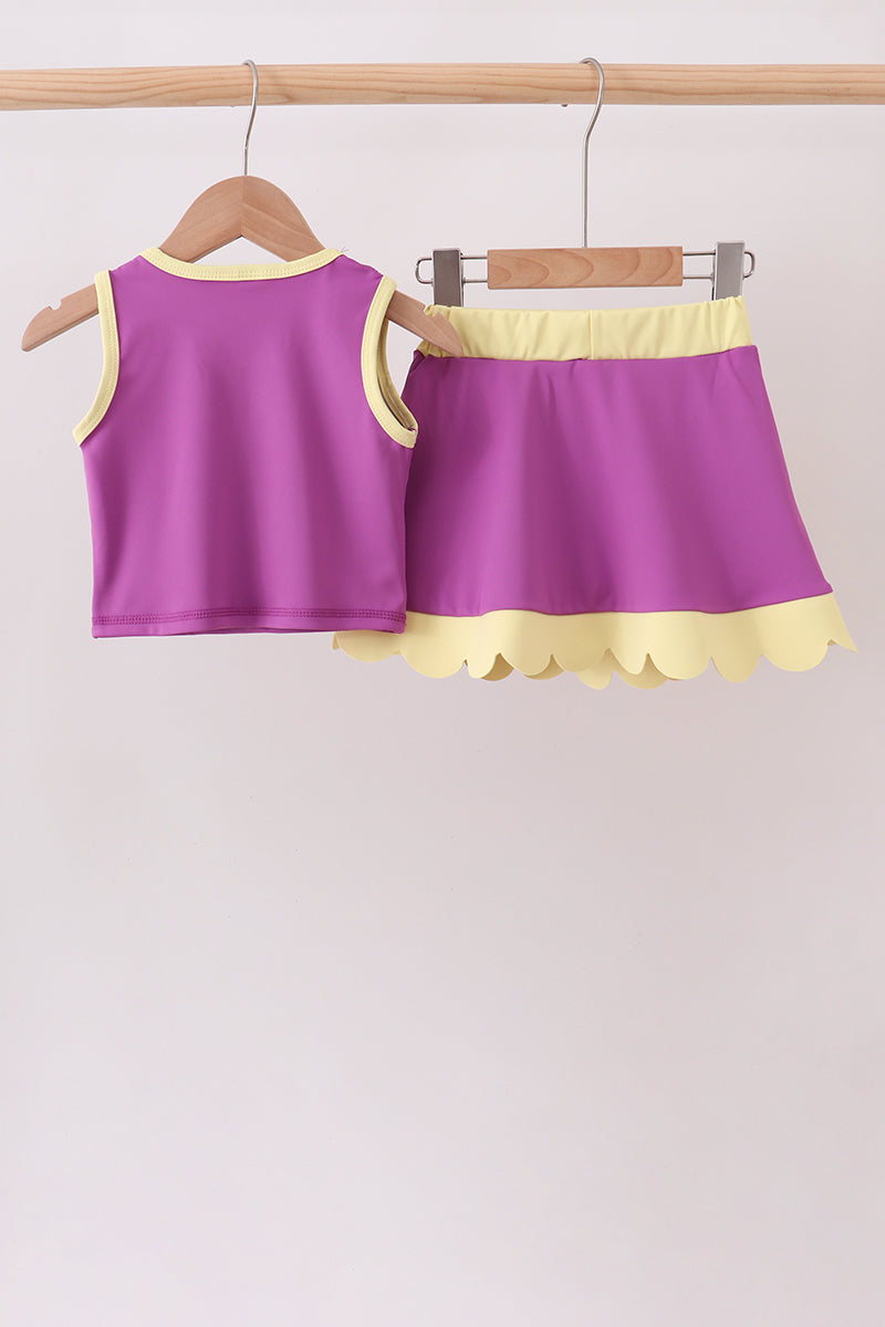 Purple top and shorts set with yellow trim on hangers against a light background