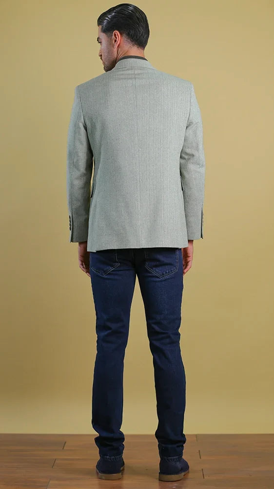 Man wearing a light gray blazer and dark blue jeans against a beige background