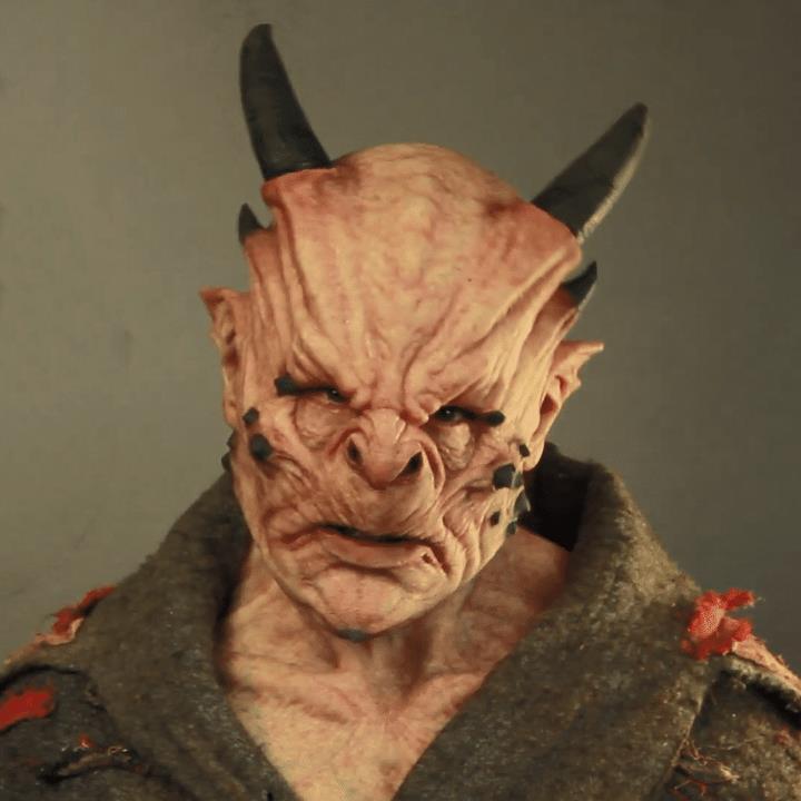 Close-up of a creature with a detailed mask and costume against a neutral background