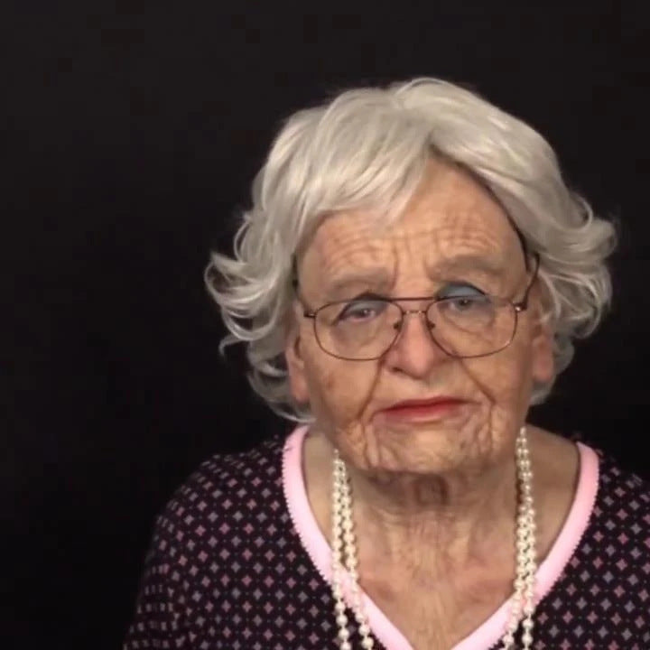 Portrait of an elderly woman with white hair and glasses against a black background