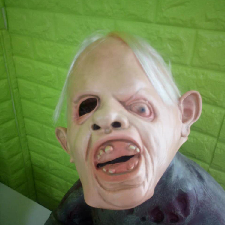Person wearing a goblin mask against a green textured wall