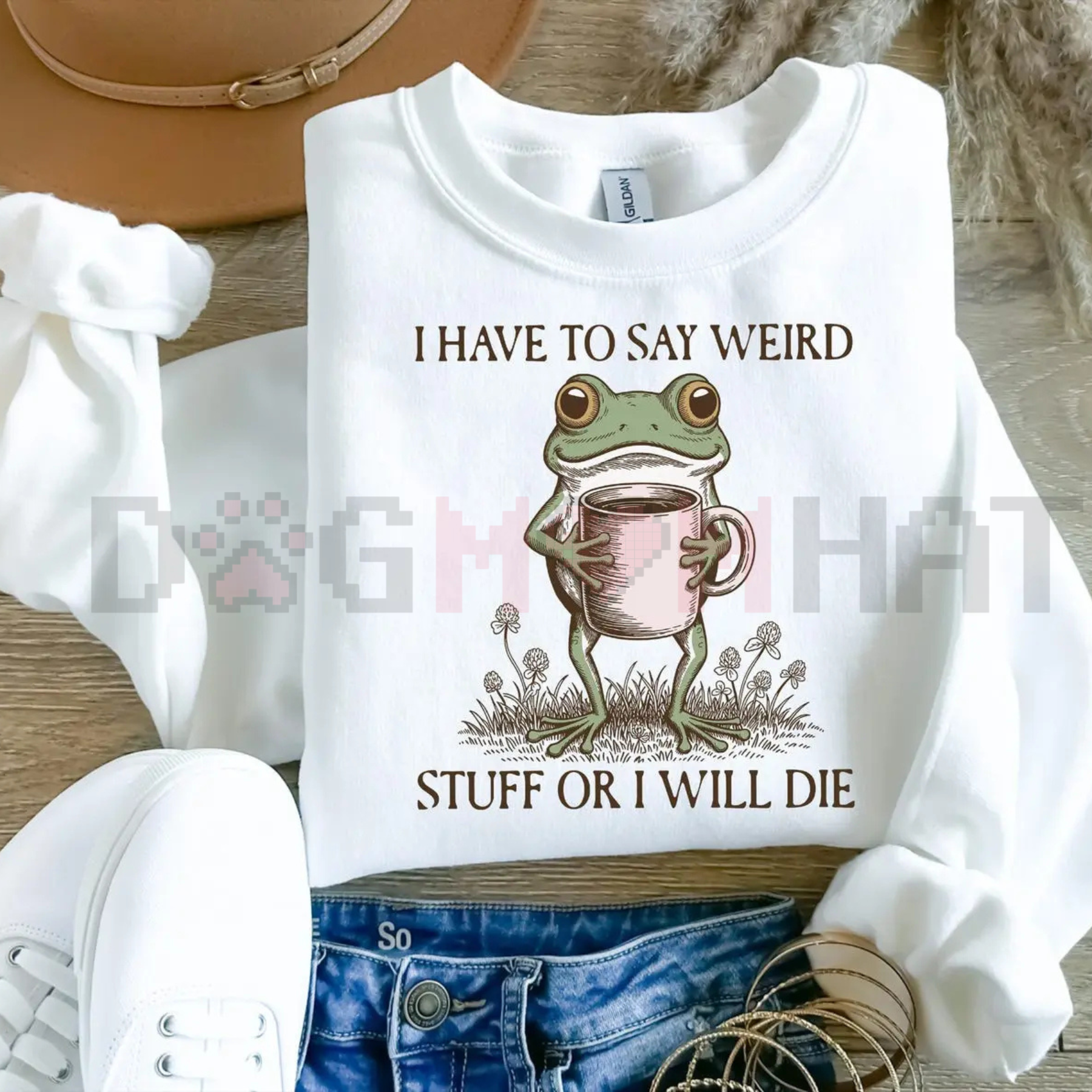White sweatshirt with a frog holding a mug and text on a wooden surface.
