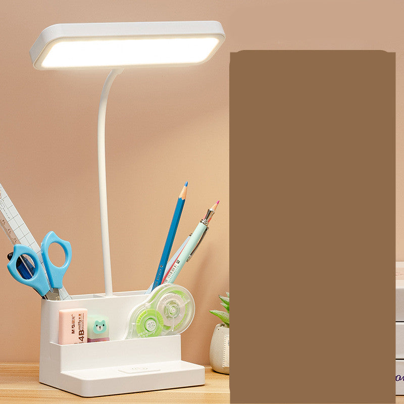 White desk lamp with a holder containing stationery items on a wooden surface.