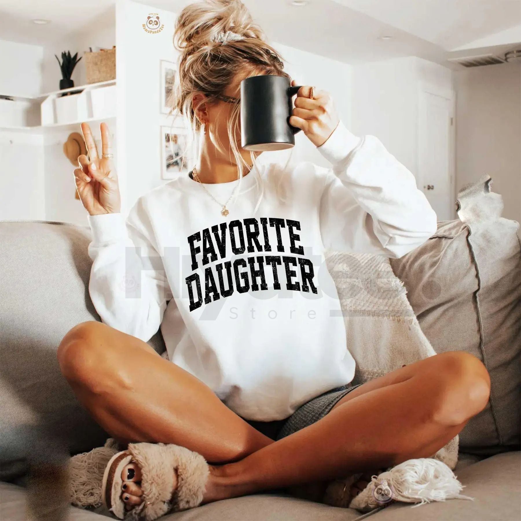 Person wearing a 'Favorite Daughter' sweatshirt sitting on a couch with a mug.