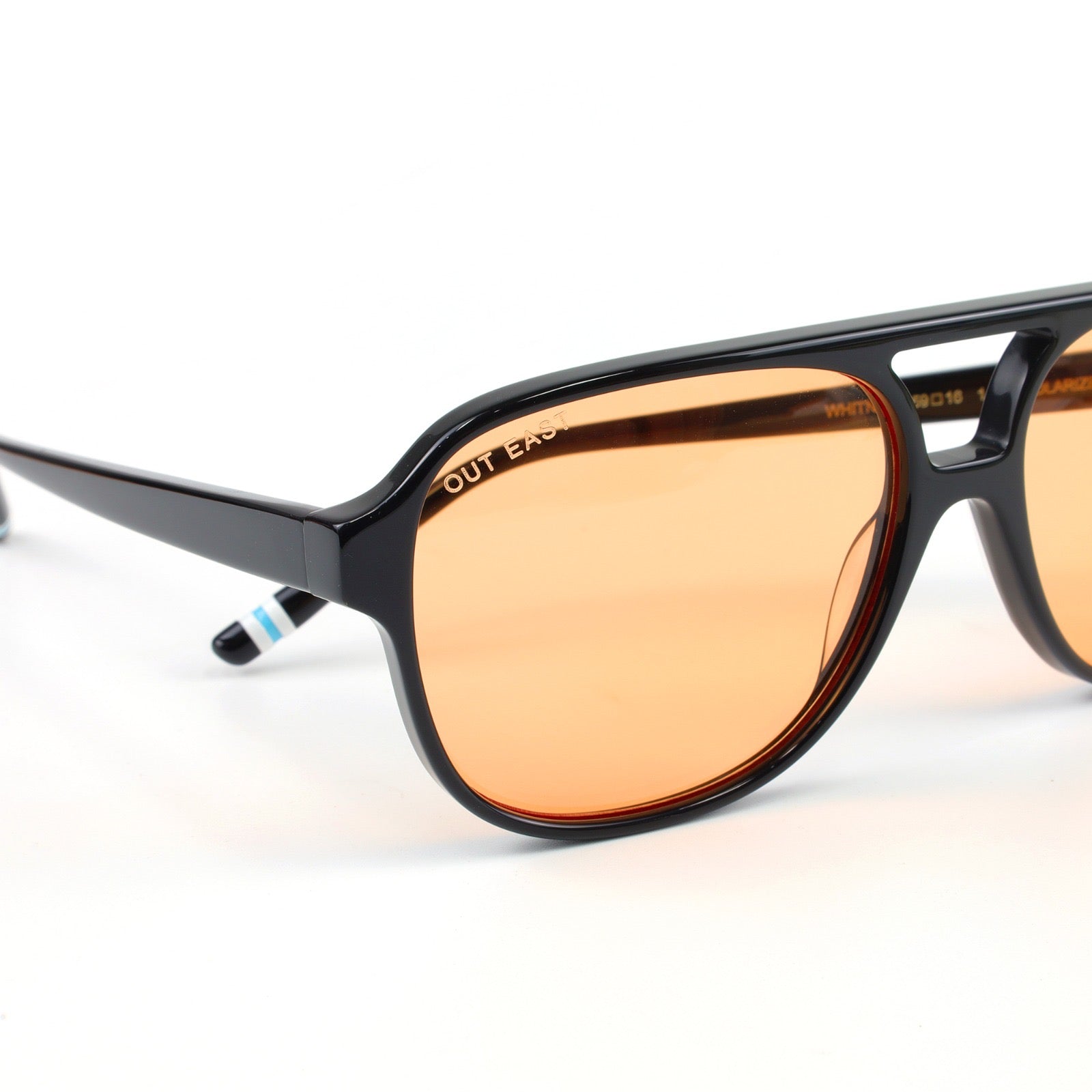 Sunglasses with black frame and orange-tinted lenses on a white background