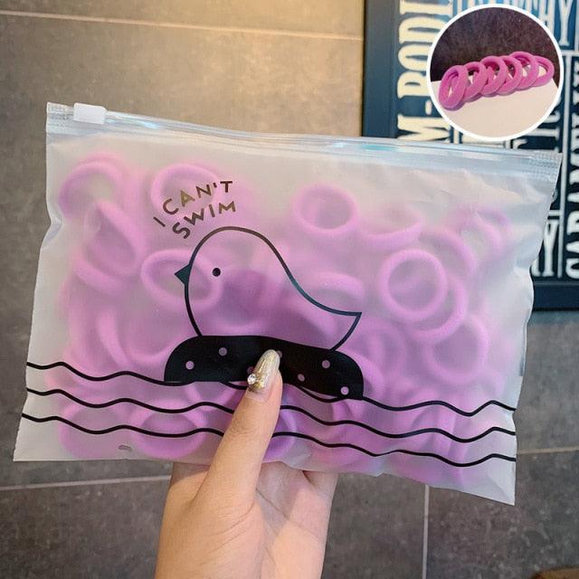 Pink rubber duckies in a clear plastic bag with a cartoon duck and 'I Can't Swim' text, held by a hand.