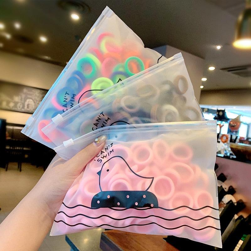 Three clear bags with colorful hair ties held by a hand in an indoor setting.