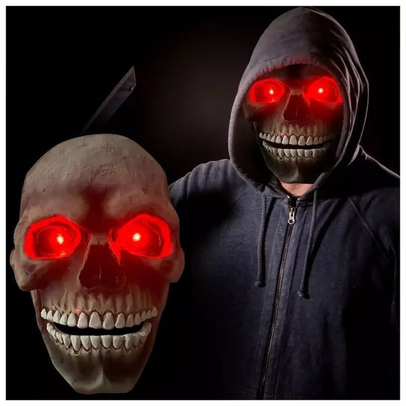 Person wearing a dark hoodie with a glowing red-eyed skull mask on a black background