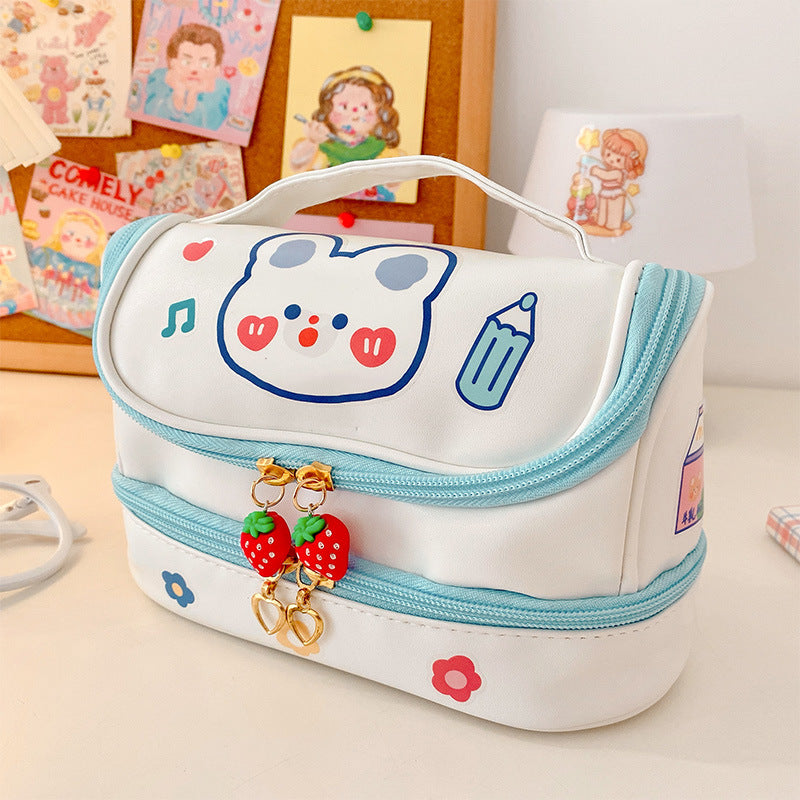White cosmetic bag with cartoon face design and strawberry charm on a desk.
